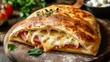 © cllareta - Delicious calzone pizza with melted mozzarella cheese and ham, served on a wooden board.