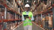 © VAKSMANV - African American young professional woman worker in hard hat uses digital tablet checks inventory walks in retail warehouse full of shelves with goods People working Distribution Center Following shot