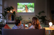 © Studio Marmellata - Two women relax on a sofa, watching a movie projected on the wall in a cozy living room. They enjoy snacks during their evening entertainment at home.