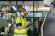 © VStudio - A woman in a yellow vest is writing on a tablet. Concept of Industry 4.0 with diverse engineers collaborating on automation technology.