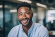 © Supanat - Portrait of a cheerful young African American man smiling confidently indoors in a modern workspace.