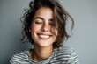 © Supanat - Bright smiling woman with wavy hair and striped shirt expressing happiness indoors.