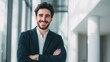 © Supanat - Smiling young businessman with crossed arms standing in modern office environment.