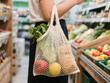 © MonTeArt - Person holding white mesh grocery bag filled with vegetables in a grocery store aisle, surrounded by fresh produce and warm lighting