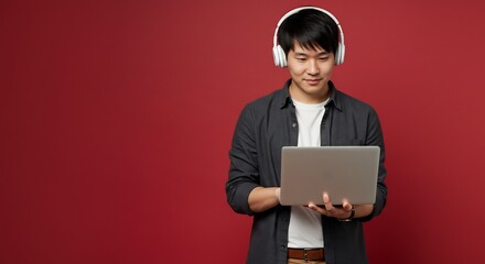 Young Asian Man with Headphones Using Laptop Computer, Red Background