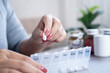 © doucefleur - close-up view of a woman organizing pills in a plastic pill box at home, preparing daily medication and vitamins for the week, showing a healthcare routine and medicine management