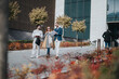 © qunica.com - Three people, two men and a woman, strolling together by a contemporary building during autumn, showcasing teamwork, professional attire, and a vibrant outdoor urban environment.