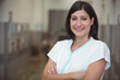 © WavebreakMediaMicro - Middle-aged female nurse standing with arms crossed in hospital hallway wearing blue-trimmed scrubs
