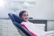 © WavebreakMediaMicro - Female child patient sitting reclined in dental chair under dental lamp wearing pink protective bib