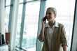 © wavebreak3 - Female business traveler talking on smartphone at airport by suitcase, glass windows, copy space
