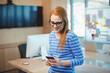 © WavebreakMediaMicro - Red-haired woman standing by wooden office desk checking smartphone with monitor and whiteboard
