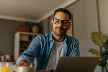 Man working from home, drinking coffee and using laptop