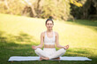 © Prostock-studio - A focused caucasian young woman athlete in a white sports bra and leggings sits cross-legged on a yoga mat, practicing meditation in a sunny, green park, outside, full length