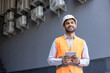 © Liubomir - An engineer in a hard hat and safety vest holds a tablet while looking up with a smile.