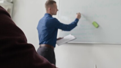 Wall Mural - Rack focus shot of male manager writing on whiteboard discussing with team weekly work plan while colleague taking notes during meeting in conference room at office
