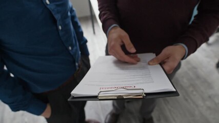 Wall Mural - Tilt up and down shot of two focused male colleagues holding clipboard discussing document with confidential corporate information while working collaboratively at modern office