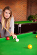 © WavebreakMediaMicro - Adult woman leaning over green-felt pool table aiming cue stick at white cue ball at bar