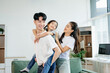 © Nuttapong punna - Asian parents and daughter enjoying a playful piggyback ride, laughing and bonding in cozy living room. Love, happiness, and family time