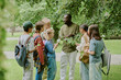 © AnnaStills - Group of diverse children and Black male teacher standing outdoors in park, teacher showing plant to students, children holding notebooks and magnifying glass, participating in educational activity