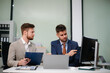 © laddawan - Professional businessmen collaborating in modern office, using laptop and tablet, discussing strategy, teamwork, and innovation.