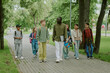 © AnnaStills - Group of diverse children walking with Black male teacher in park, teacher holding laptop, children talking and smiling, multiethnic group including boys and girls, outdoor education setting