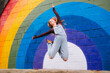 © Westend61 - Woman jumping joyfully in front of colorful rainbow mural outdoors
