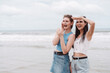 © Kiattisak - Two young women friends smiling and looking out at the ocean while standing on the beach. Perfect summer vacation vibe showing friendship, fun, freedom, and joyful outdoor lifestyle.