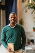 © PintoArt - Smiling black teacher holding notebook in modern classroom