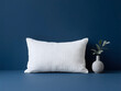 © Tetiana Kosharska - Rectangular white pillow with subtle woven pattern and small ceramic vase with greenery on dark blue backdrop in bright minimal decor