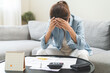 © KMPZZZ - Debt and financial concept, stressed asian young woman have a headache while sitting on sofa calculate expenses, income, looking bills of credit card for prepare payment or pay bills on table at home.