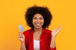 © Anastasiya - Smiling African American woman holding credit card and raising her hand in excitement. Financial freedom and digital payment concept on yellow background, copy space
