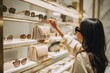 © Cheewarat - over-the-shoulder view of woman reaching for sunglasses on shelf in luxury tax-free shop, minimal modern decor, retail travel moment