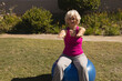 © WavebreakMediaMicro - Senior woman balancing on blue stability ball on backyard lawn, extending arms forward at shoulders