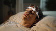 © Prostock-studio - A man lies comfortably in bed with his eyes closed during a hypnosis session aimed at addressing his sleep issues. A device gently illuminates his forehead, suggesting focused relaxation.
