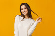 © Prostock-studio - Smiling brunette girl flirting and touching her long beautiful hair over yellow background, playful woman looking at camera, empty space