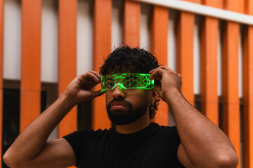 Young latin software developer adjusting his futuristic neon green smart glasses in front of an orange building