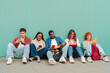 © Jose Calsina - Cheerful group of young friends interacting with their mobile devices, sharing moments and laughter while sitting on the ground, showcasing a modern lifestyle of connectivity and friendship.