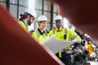 © AU USAnakul - Group of engineers discussing blueprint in front of robotic arms in a modern industrial factory, representing teamwork in smart manufacturing, Robotics factory planning,
