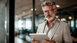© Phichitpon - Busy mature older business man executive standing in office using digital tablet. Middle aged professional businessman corporate manager wearing suit