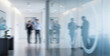 © Renderis - Blurred figures in a modern office corridor with glass walls and artwork.