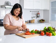 © Yolania - Smiling Asian woman slicing vegetables for a clean eating diet plan in a minimalist modern kitchen