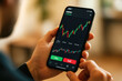 © DailyStock - Person holding smartphone displaying financial trading chart with buy sell buttons