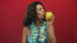© Krakenimages.com - Woman wearing a lei and bikini joyfully holding a yellow piggy bank against a vibrant red background, showcasing a playful and tropical savings concept.