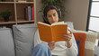 © Krakenimages.com - Woman reading book on couch wearing headphones in cozy living room with bookshelves and pillows, enjoying a peaceful moment indoors.