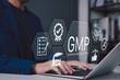 © Supatman - Good Manufacturing Practice (GMP) Concept. Businessman working on laptop with icons representing compliance, quality control, assurance, certification, manufacturing standards in corporate setting,