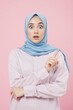 © lina - Surprised young woman in hijab pointing upwards with a questioning expression.