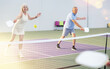 © JackF - Concentrated experienced team of pickleball players, aged woman and man, preparing to strike and return ball to opponents field during doubles match on indoor court