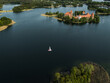 © AmazingAerialAgency - Aerial view of Trakai Island Castle, a medieval castle, stands in stark contrast to the dark water, with a lone sailboat nearby, Trakai, Vilnius country, Lithuania.