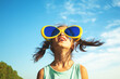 © vvvita - Little girl with big, funny sunglasses enjoys the sun. The girl against the blue sky on a sunny day. Summertime, Party, Travel concept