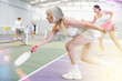 © JackF - Focused active aged woman playing friendly pickleball match on indoor court. Senior people sports concept..
